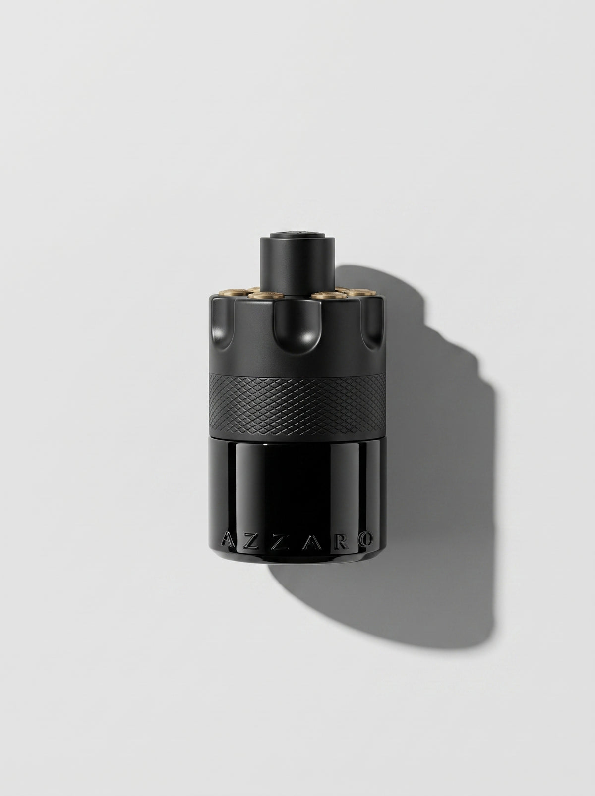 Azzaro Most Wanted — matte black cylinder with a knurled band and gold-topped studs, top-down